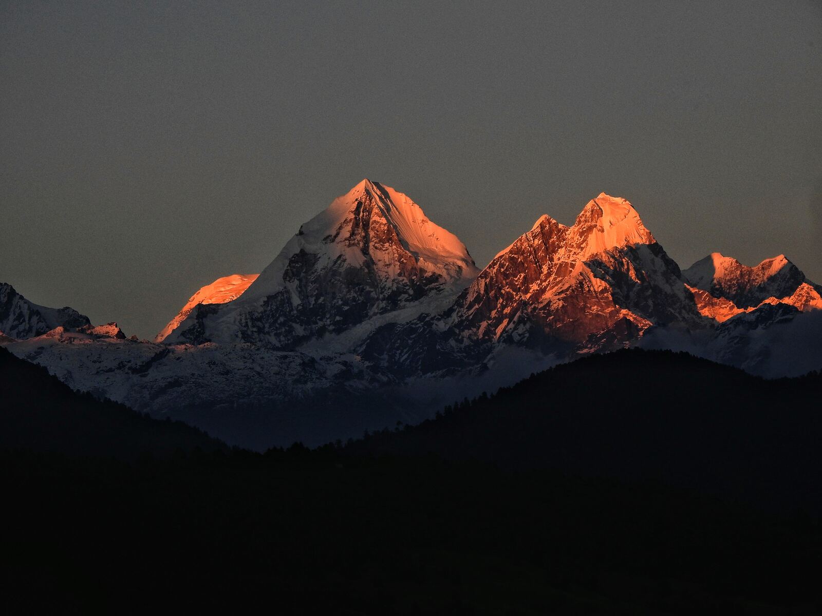 Snow peaks glowing orange at sunrise above a dark ridge